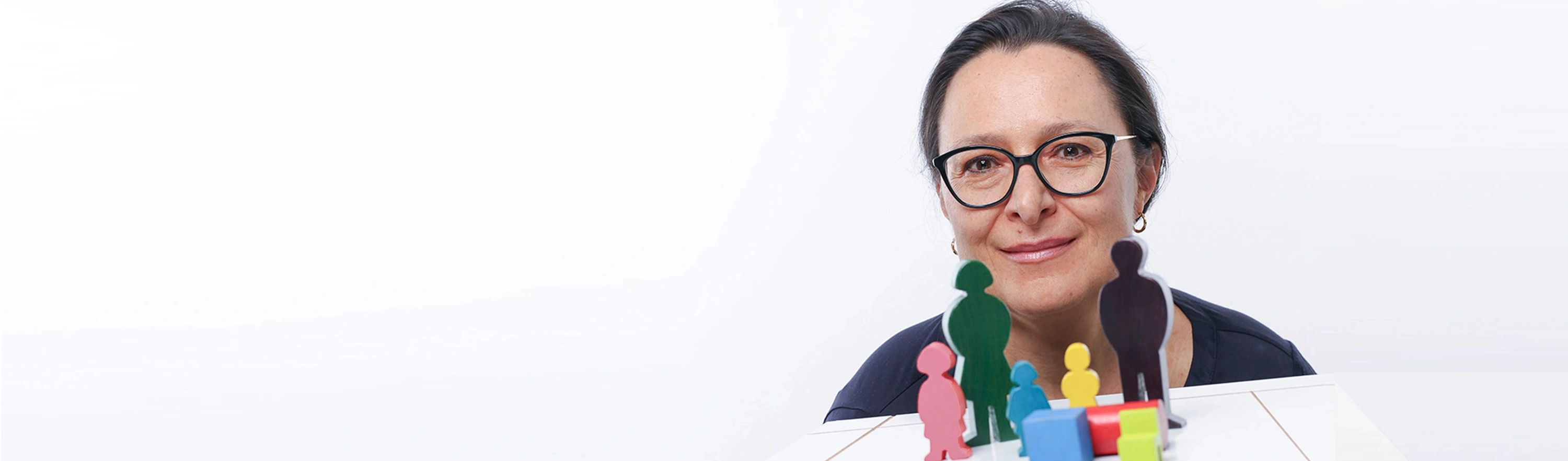 Frau Mag. Ritter-Venier lächelt hinter einer Mehrpersonen-Aufstellung mit Holzfiguren hervor